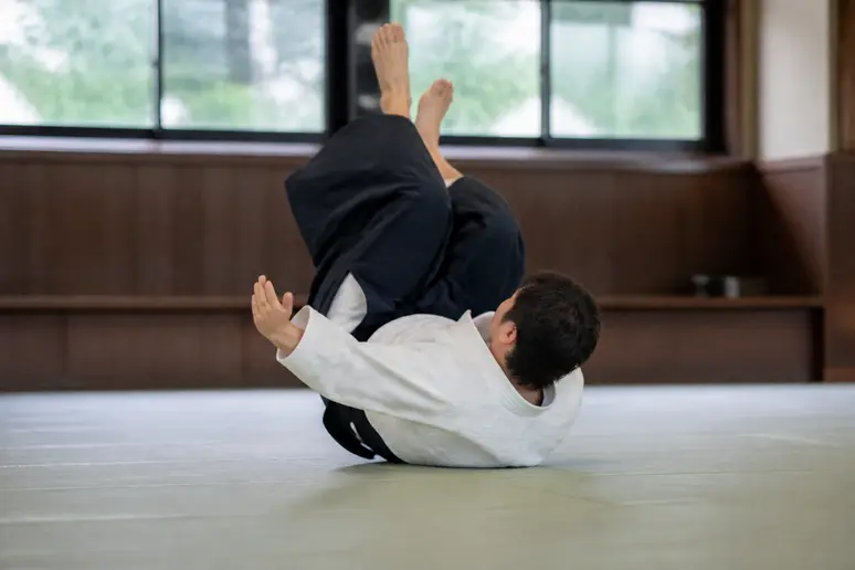 Pratiquant effectuant une roulade arrière maîtrisée pour amortir une chute sur un tatami.