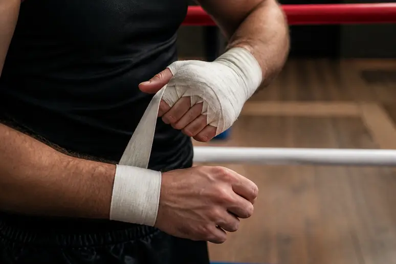 Mains d'un boxeur entourées de bandes de protection en coton blanc dans une salle de sport.