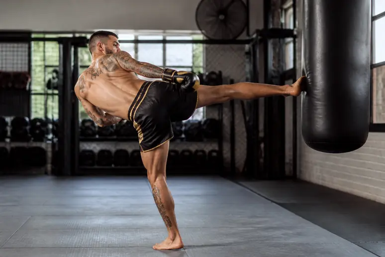 Kickboxeur effectuant un low-kick avec une rotation précise du pied d'appui sur le tapis du gymnase.