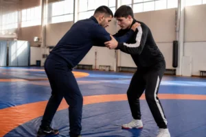 Deux sportifs en tenue travaillent une prise de lutte greco romaine sur un tapis dans un gymnase.