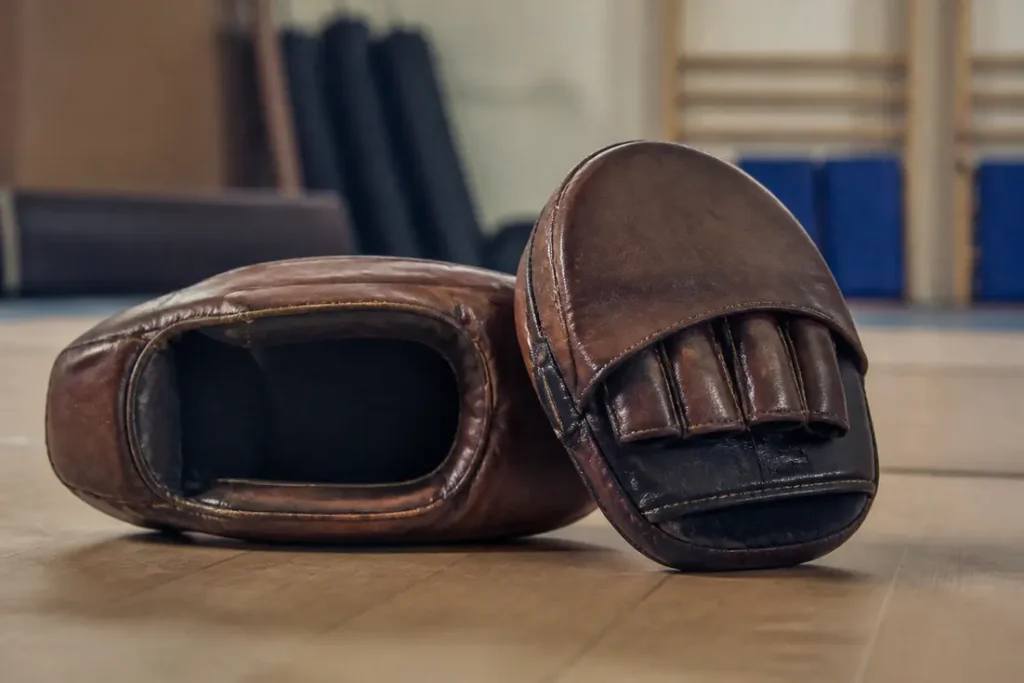 Paire de pattes d ours boxe en cuir, posées sur un tapis de tatami dans un dojo d'arts martiaux.
