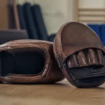 Paire de pattes d ours boxe en cuir, posées sur un tapis de tatami dans un dojo d'arts martiaux.