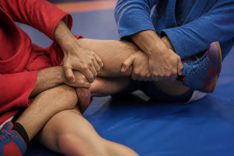 Mains d'un pratiquant de Sambo effectuant une saisie de jambe pendant un entraînement.