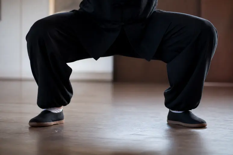 Personne en posture basse de Tai Chi, genoux pliés au-dessus des orteils, ancrage au sol.