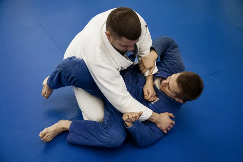 Deux pratiquants en tenue de sport travaillant une technique de contrôle au sol sur tatami.