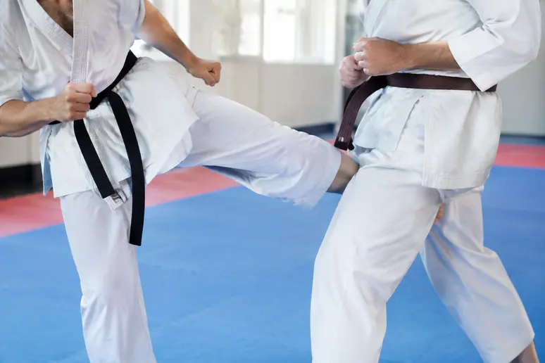 Pratiquant de sports de combat exécutant un low kick sur la cuisse d'un partenaire en dojo
