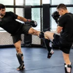 Deux pratiquants de sports de combat effectuent un blocage de calf kick dans une salle d'entraînement.