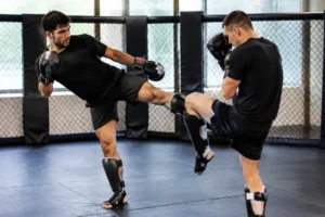 Deux pratiquants de sports de combat effectuent un blocage de calf kick dans une salle d'entraînement.