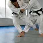 Deux pratiquants en kimono blanc réalisent un ko soto gari lors d'un entraînement de judo.