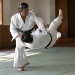 Entraînement de judo sur tatami illustrant le mouvement technique du koshi guruma entre deux pratiquants.