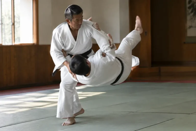 Entraînement de judo sur tatami illustrant le mouvement technique du koshi guruma entre deux pratiquants.