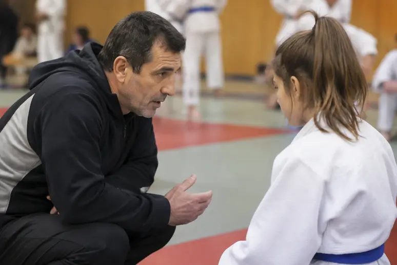 Entraîneur de judo analysant une technique sur le tatami pour guider un jeune pratiquant.