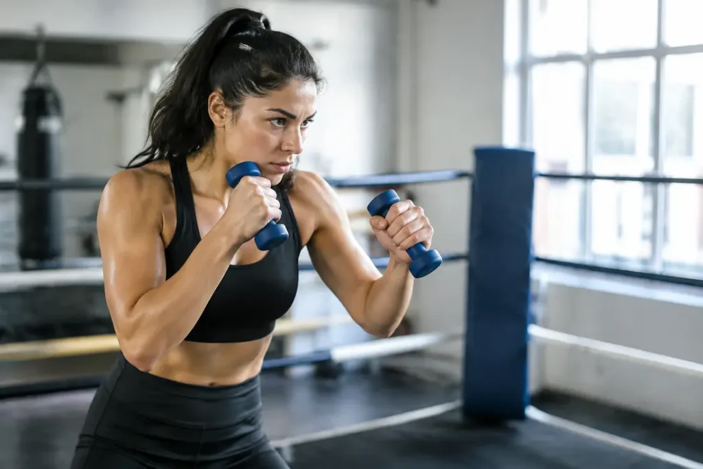 Pratique de shadow boxing avec des haltères pour renforcer sa garde boxe en salle.