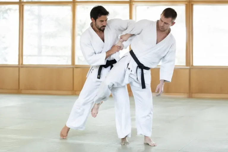 Pratiquants d'arts martiaux en plein entraînement réalisant la technique de projection hiza guruma dans un dojo lumineux.