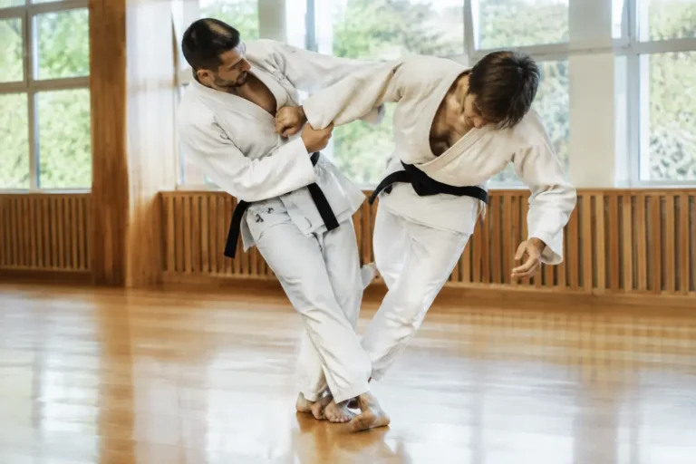 Deux pratiquants de judo exécutent un sasae tsurikomi ashi sur un tatami lumineux.