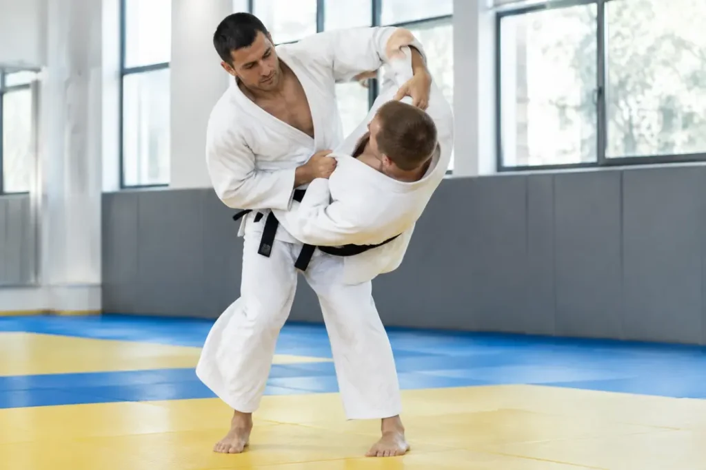 Deux judokas en kimono blanc pratiquent le tsurikomi goshi sur les tatamis d'un dojo lumineux