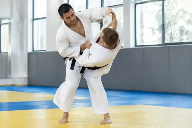 Deux judokas en kimono blanc pratiquent le tsurikomi goshi sur les tatamis d'un dojo lumineux